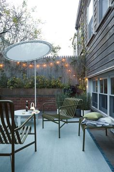 two chairs and an umbrella are on the back patio with string lights strung around them