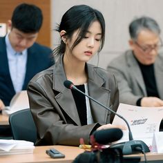 two people sitting at a table with microphones in front of them and papers on the table