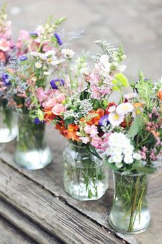 four glass vases filled with colorful flowers on top of a wooden table next to each other