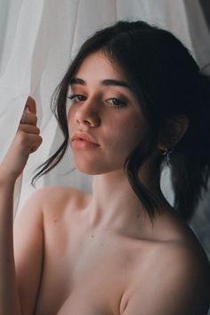 a naked woman is standing in front of a white curtain and holding her arm up