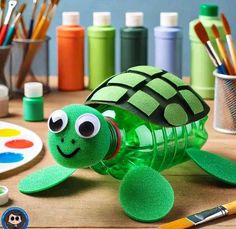 a turtle made out of plastic bottle sitting on top of a table next to paintbrushes