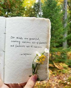 someone holding up a book with a quote on it in the woods near some trees