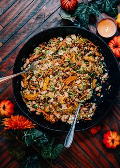 a pan filled with food on top of a wooden table next to flowers and candles