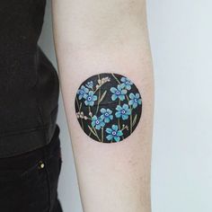 a small blue flower tattoo on the left inner forearm and arm, next to a woman's black shirt