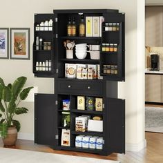 an open cabinet in the corner of a room next to a potted plant and pictures on the wall