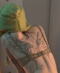 a woman with tattoos on her back wearing a green hat