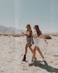 two women walking in the desert with wind mills behind them