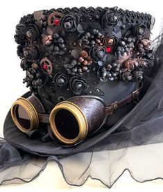 Steampunk Madhatter Hand made In black colour silk fabric Top Hat with leather covered embossed gears goggles with Red lens dial with 3D roses with Victorian brass embellishments angles on roof and black with net bows and bustle at the back of hat.  Please refer to the photos. The hat is lined with black satin. Front has copper Jewel cogs Details With Antique brass buckle.  Size Available in 55cm Please note this is full head hat and not mini hat)  Height of hat 18cm Thank you for looking Steampunk Black Costume Hat For Festivals, Steampunk Black Costume Hats And Headpieces For Festivals, Vintage Black High Crown Costume Accessories, Black Steampunk Costume Hats And Headpieces, Black Steampunk Costume Accessories For Themed Events, Vintage Black Costume Accessories For Themed Events, Custom Black High Crown Top Hat, Custom Black Top Hat With High Crown, Vintage Black Costume Hats For Themed Events