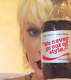 a woman holding up a bottle of soda with an ad on the label that says, we never go out of style