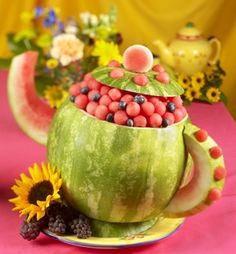 a watermelon teapot with berries in it and sunflowers on the side