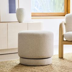 a white vase sitting on top of a wooden table next to a chair and ottoman