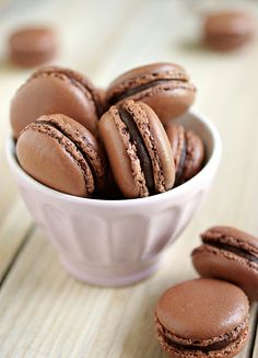 a white bowl filled with chocolate macaroons on top of a wooden table next to cookies