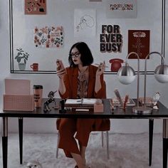 a woman sitting at a desk holding up her cell phone