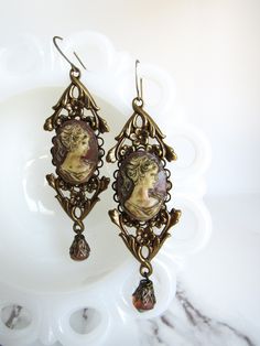 These Victorian-style LARGE earrings are made with 1960s vintage resin cameos (originally bright salmon pink and white) have been hand-patinaed by me for that lost-antique look. The cameos are set against Victorian style brass stampings, and are accented with dark salmon Czech glass beads. These earrings are " long from the top of the earring hook to the bottom of the dangles. Without the hook, they are " long. The matching brooch can be found here: ------------------- **Please be sure to read my shipping and store policies, and don't hesitate to send me a message with any questions you may have! INTERNATIONAL BUYERS: Please be aware that there may be taxes or customs fees that are not included in the purchase price. I cannot reimburse for additional fees. Victorian Style Jewelry, Victorian Cameo, Vintage Style Earrings, Earring Hook, Salmon Pink, Large Earrings, Style Earrings, Victorian Style, 1960s Vintage