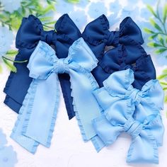 three blue bows are sitting next to each other on a white surface with flowers in the background