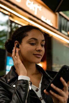 a woman is using her cell phone and listening to earbuds on the street