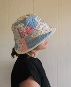 a woman wearing a hat with patchwork on the brim and side, standing against a white wall