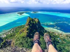 a person's feet are on the edge of a cliff overlooking an island and lagoon