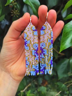 a person holding up some kind of beaded earring in their left hand and green leaves behind them