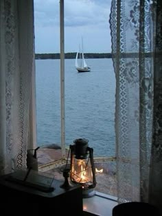 a lamp is sitting on the window sill by the water with a sailboat in the distance