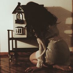 a woman sitting on the floor in front of a doll house with her head down