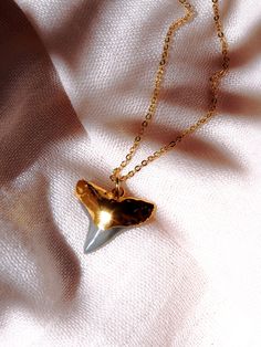 A gorgeous gold shark tooth necklace. A single black shark tooth dipped in gold and strung on a gold filled chain. Lovely, striking, and unique. Perfect alone or as a lovely layered necklace. Handmade on Maui, Hawaii. ✦ DETAILS ✦✧ Name: Mano Niho Kahi Black (mah NO-NEE ho-KA-hee) - Shark with one tooth.✧ Genuine fossil shark tooth; plated in 18kt gold.✧ 14kt gold filled chain.✧ 14kt gold filled spring clasp.✧ Due to the nature of the shark tooth, each piece will vary in size and shape. Every sha Shark Tooth Necklace Gold, Ethereal Ocean, Shark Teeth Jewelry, Hawaii Necklace, Tooth Jewelry, Surf Necklace, Shark Tooth Pendant, Tooth Pendant, Hawaii Jewelry