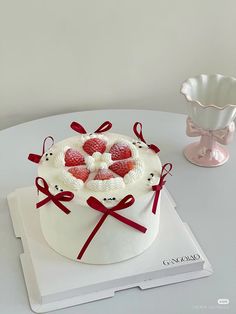 a white cake decorated with strawberries and bows on top of a table next to a vase