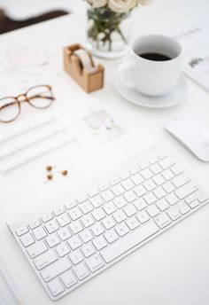 a white keyboard sitting on top of a table next to a cup of coffee and glasses