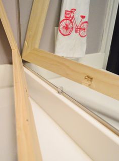 a bathroom mirror sitting next to a white bath tub under a wooden framed mirror on top of a wall