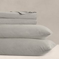 two pillows sitting next to each other on top of a white bed sheet covered in grey and white striped sheets