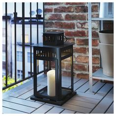 a lit candle sitting on top of a wooden table next to a brick wall and railing