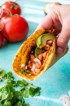 a hand holding a tortilla filled with beans, avocado and tomatoes