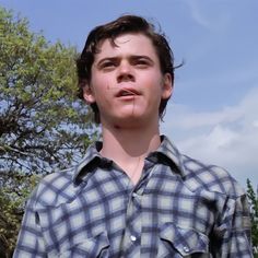 a young man standing in front of a tree with his tongue out and looking at the camera