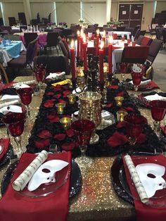 the table is set with red and black plates, napkins, silverware, and candles