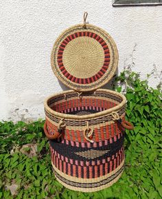 two woven baskets sitting on top of grass next to a white wall and green plants