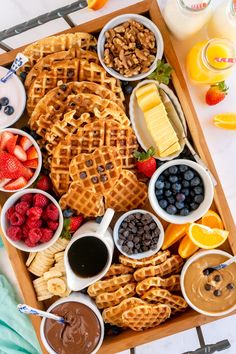 a wooden tray filled with waffles, fruit and other foods on top of a table