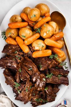 a white plate topped with roast, potatoes and carrots next to a spoon on a table