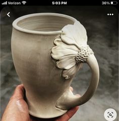 a hand holding a ceramic mug with a flower on it