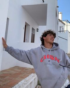 a young man standing in front of a white building with his arms out and smiling