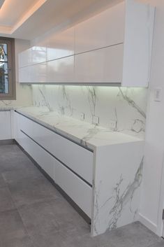 an empty kitchen with white cabinets and marble counter tops in front of a large window