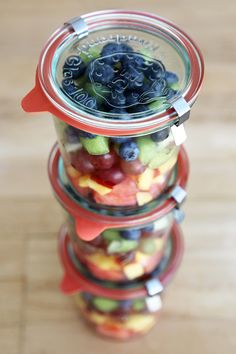 three glass jars filled with fruit sitting on top of a wooden table