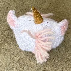 a knitted unicorn hat with a gold horn on it's head sitting on the floor