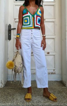 a woman standing in front of a door wearing white pants and a crochet top