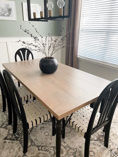 a dining room table with chairs and a vase on it's centerpiece in front of a window