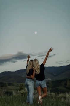 two women are standing in the grass with their arms up and one is pointing at the sky