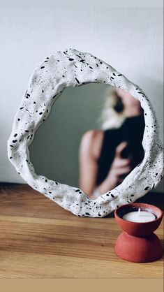 a mirror sitting on top of a wooden table next to a red vase and candle