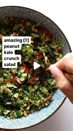 a bowl filled with lots of food on top of a white countertop next to a hand holding a wooden utensil