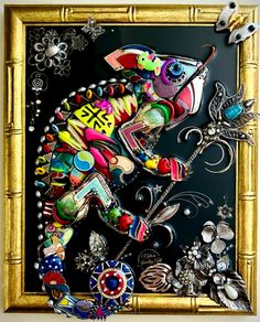 a colorful fish is on display in a gold frame with beads and other items around it