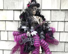 a skeleton wearing a witch costume hanging on the side of a house with purple and black decorations