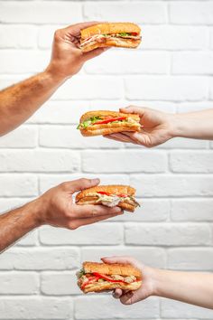 four hands holding sandwiches in front of a brick wall